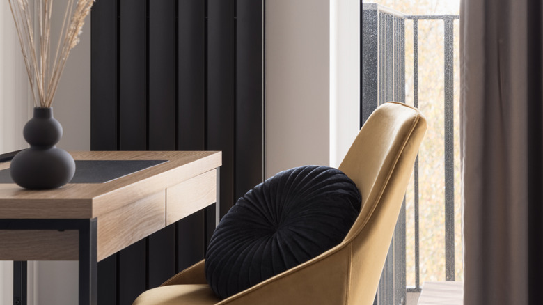 Aynı renkte bir vazo bulunan bir masanın arkasında siyah dikey bir radyatör