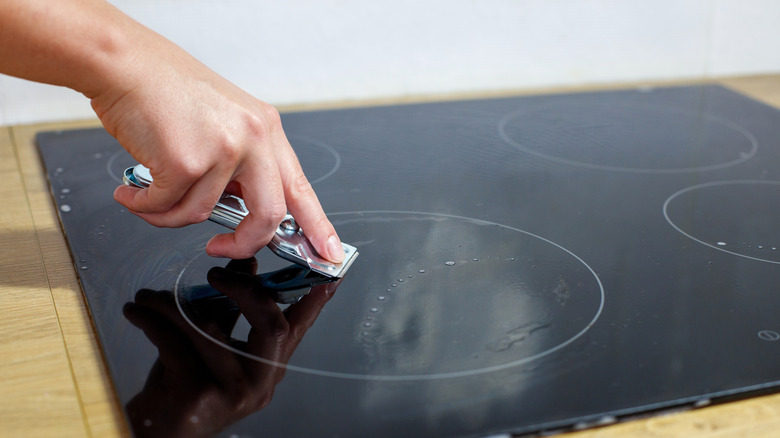 Cam ocağı kapalı lekeleri temizlemek için jilet bıçağı kullanan kişi