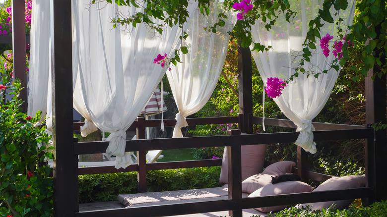 Yatak ve beyaz perdeler ile açık bir uyku sundurma.