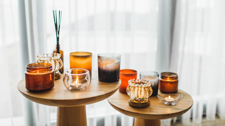 Konforlu koltuk yakınındaki ahşap çay masasında kahverengi kaselerde farklı cam şamdan organik soya mum mumları.