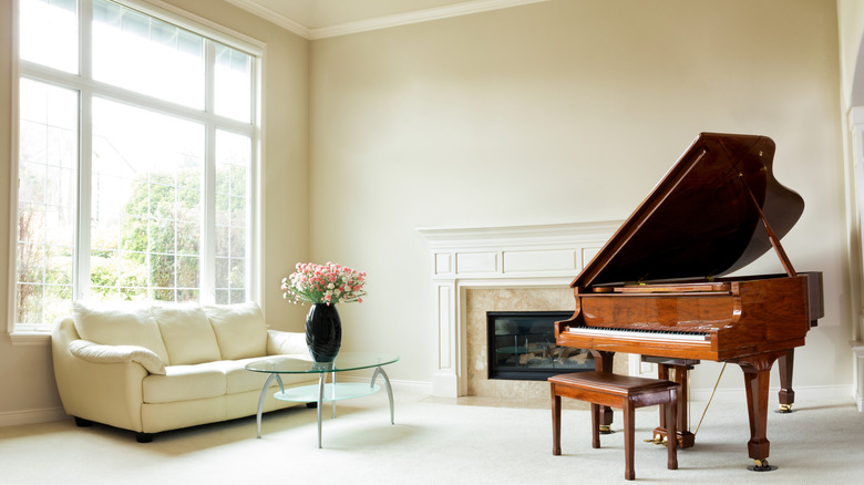 Grand piyano, şömine, kanepe ve parlak gün ışığı ile büyük pencere ile oturma odası.