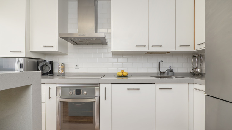 Yansıtıcı beyaz karo backsplash, gri tezgah ve paslanmaz çelik aletlere sahip modern küçük bir mutfak.