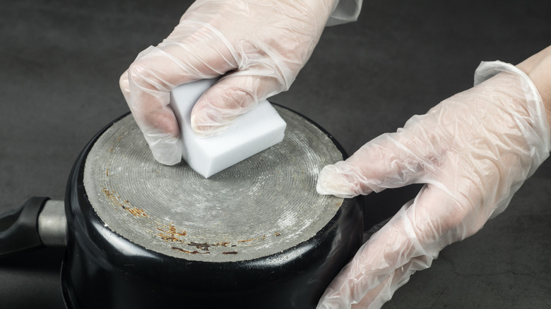 Bir tavada bir temizleme silgisi kullanarak eldivenli el