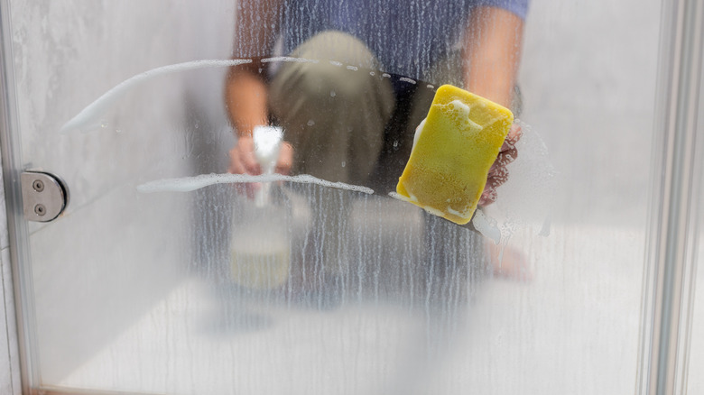 Duş kapısından sert su lekelerini siliyor kadın