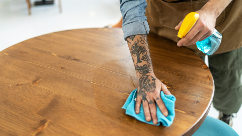 Dövmeli eli olan bir kişi, bir paçavra ile ahşap bir masa üstünü temizler