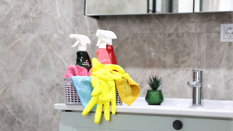 Tezgah üzerinde bir sepet temizleme malzemesi ve sarı eldiven ile mermer banyo
