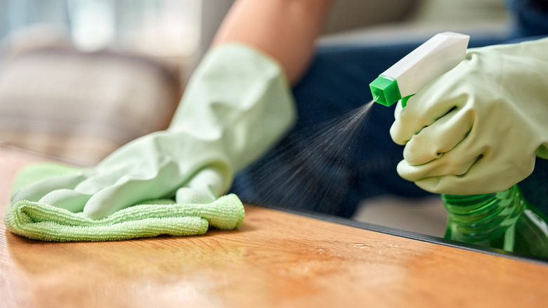 Ahşap masaya temizleyici püsküren ve bez tutan bir kişi