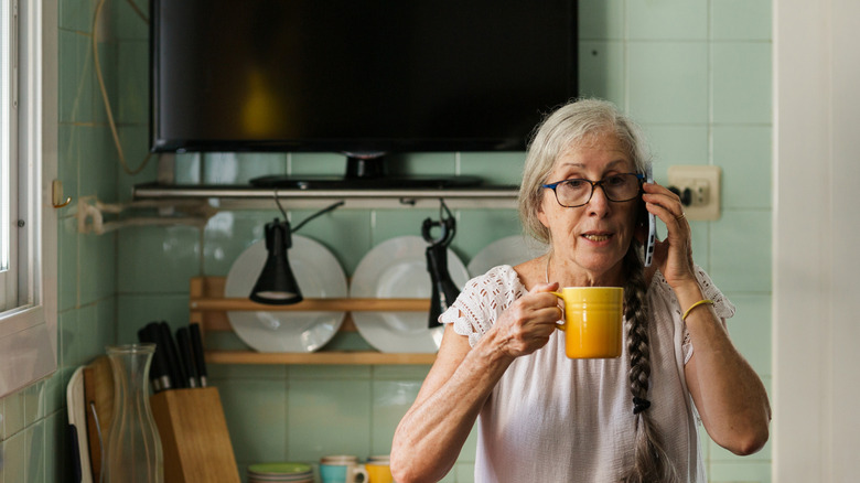 Onun arkasında bir televizyon ile mutfağında kahve içen kadın