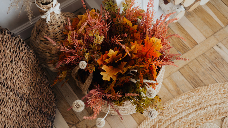 Yeşillik ve diğer kurutulmuş ve sahte seçimlerle bir şömine yakınındaki yerde bir sonbahar sepeti