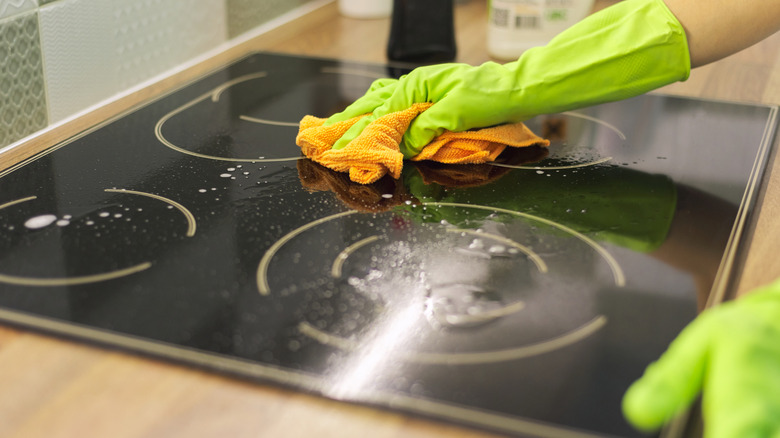 Siyah bir ocakın yakın çekimi, bir mikrofiber bez kullanılarak yeşil eldivenlerde bir dizi elle temizleniyor