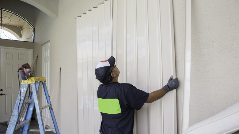 Bir yüklenici, yeni inşa edilmiş bir evin giriş yolunda büyük bir depolama dolabının üzerine beyaz bir akordeon kapısı kurar.