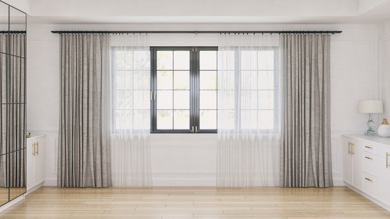 Her iki tarafta alçak beyaz parke dolapları olan rahat bir retro-şık zarif kaplamasız iç mekanın önden görünümü, pervazlar ve dekorasyonlu beyaz ahşap panelli bir duvarın önünde büyük ve yüksek ayna dolabının önünde.