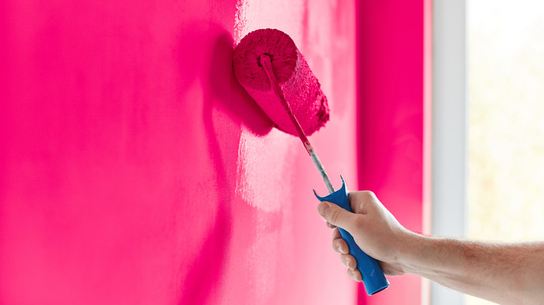 Bir adamın eli, bir oda sıcak pembesi boyamak için bir silindir kullanır
