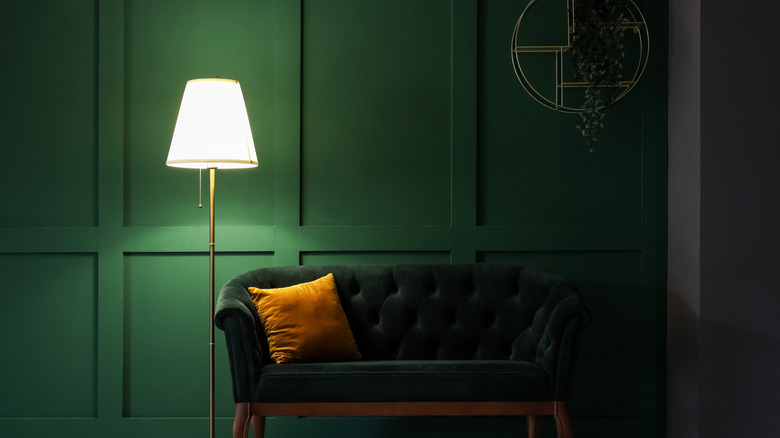 Bir kanepe ve lambanın arkasında orman yeşil bir duvar.