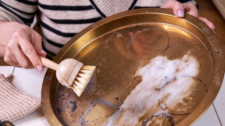 Beyaz macun ve ahşap bir fırça ile bakır tepsisini temizleyen bir kişi