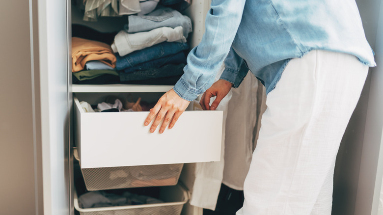 Dolabında beyaz bir çöp kutusundan giyim eşyalarını çeken bir kadın