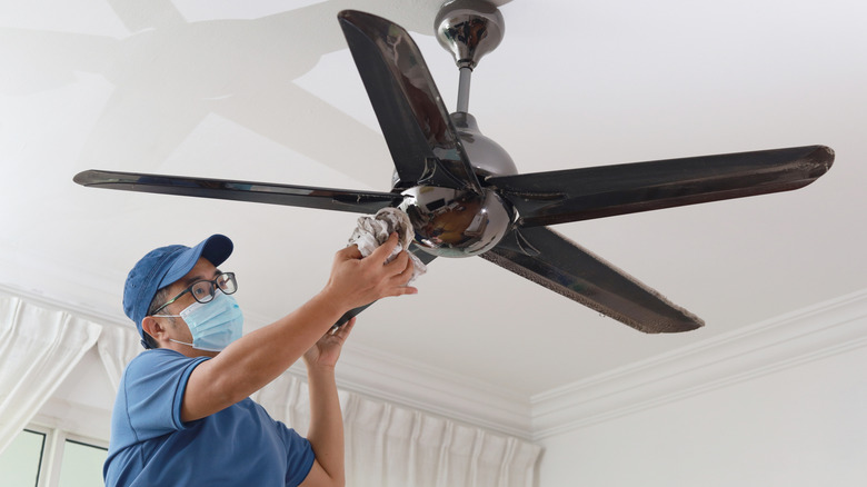 Maske takan bir tavan fanı temizleyen adam