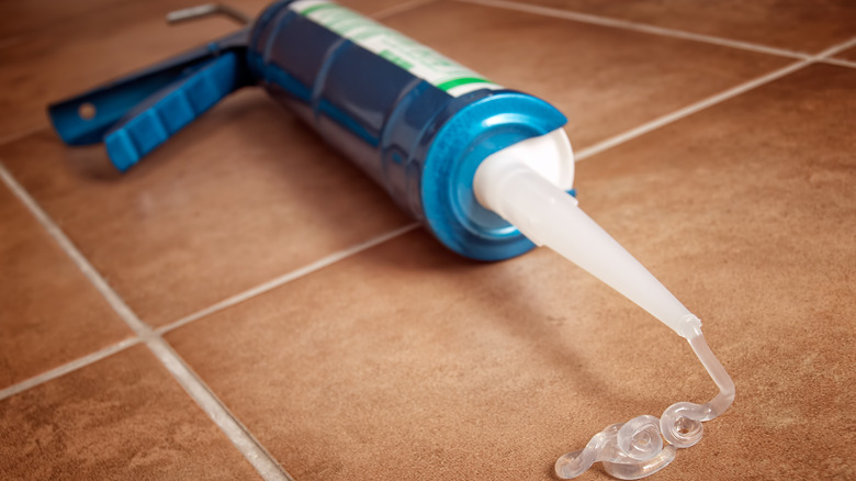 Berrak silikon kalafat mavi bir kalafat tabancasında bir tüp üzerindeki bir nozuldan sızar.