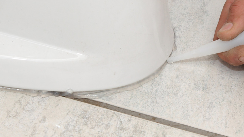 Bir kişi dağınık bir şekilde tuvalet tabanının etrafına açık kalafat uygular.