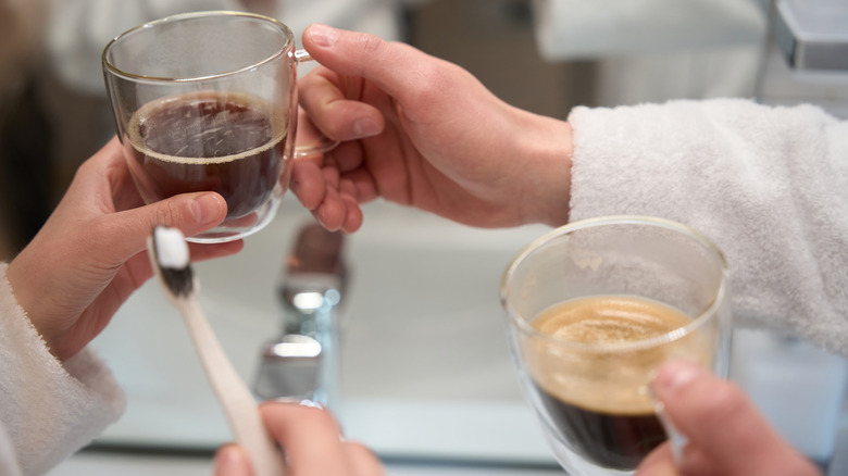 Bir kişi bir kahve kupası tarafından diş fırçası tutar