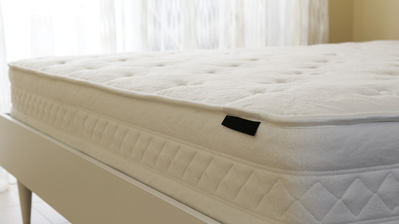 Arka planda saf perdeler ile akıllı beyaz yatak çerçevesinde beyaz çıplak yatak