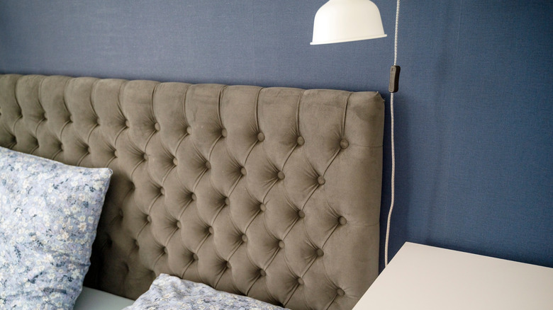 Kahverengiye kapitone bir kumaş headborad'ı mavi bir duvar ve arkasında okuma lambası ile kapatın.