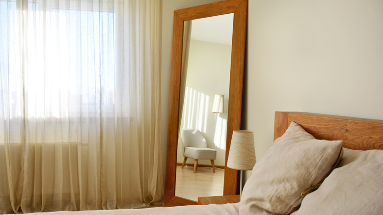 Bir yatak odasının köşesinde şeffaf perdeler ve yanında bir pencere bulunan büyük bir ayna.