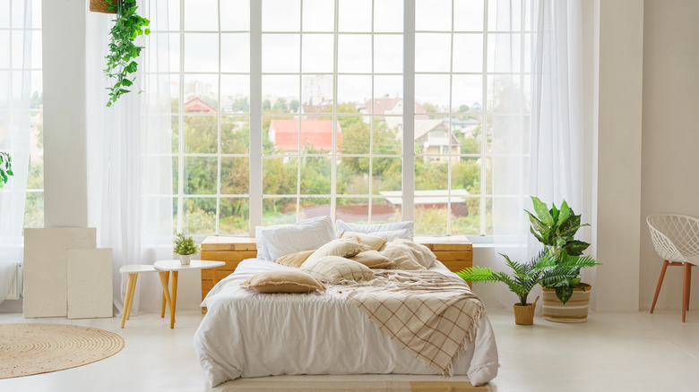 Zeminden tavana yatak odası pencereleri, önlerinde çift kişilik yataklı ve beyaz yataklarla oluşan beyaz panellere sahip.