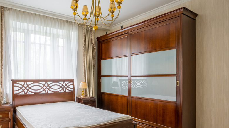 Eşleşen başucu masalarına sahip ahşap bir çerçevede çift kişilik yatağın yanında şeffaf panellere sahip büyük bir ahşap gardırop.