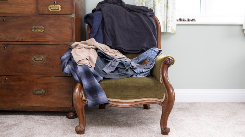 Arkasında ahşap bir çekmeceli antika koltukta kıyafet yığını.