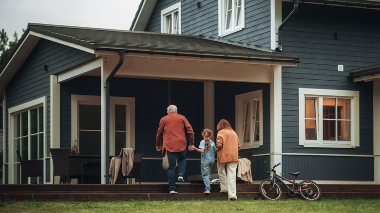 Sandalyeli bir ön sundurma ve eve yaslanmış bir bisikletle yürüyen aile