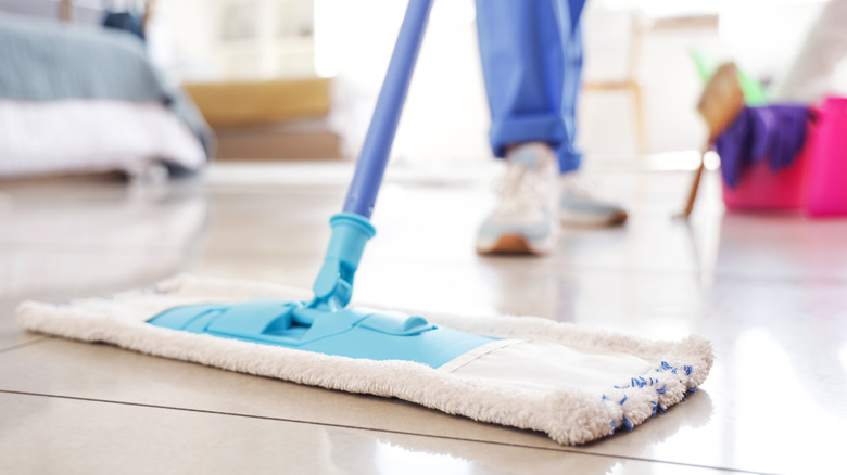 Açık renkli karo zeminde düz mikrofiber paspas kullanan bir kişi