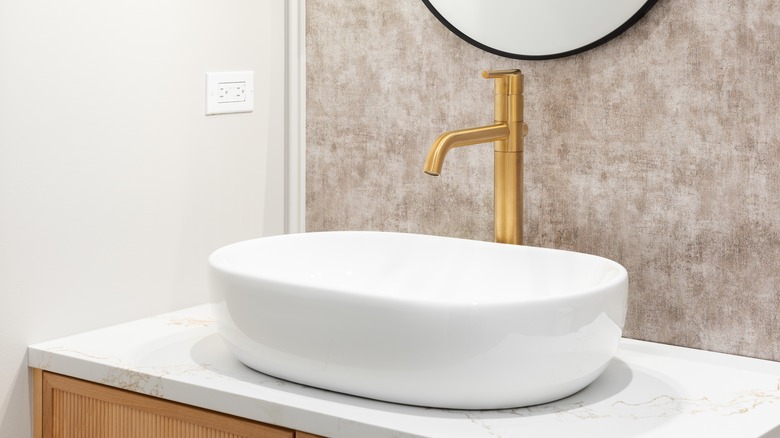 Beyaz lavabo, altın musluk ve dokulu zeminli banyo