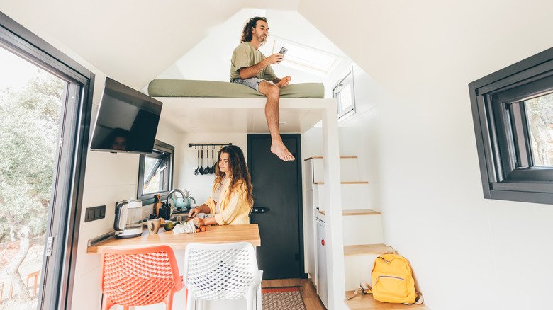 Genç bir kadın mutfakta çalışıyor, bir erkek küçük bir evin çatı katında otururken