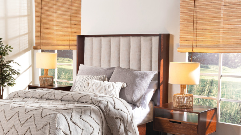 Yivli kumaş dokusu ve koyu ahşap çerçeveli bir başlık içeren iki pencere arasına yerleştirilmiş yatak