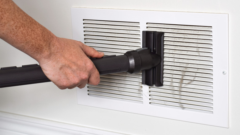 Bir kişi bir hava havalandırmasını temizlemek için bir vakum ve ek kullanır