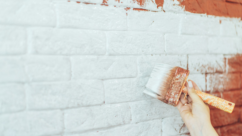 Bir kadının elinin yakı bir tuğla duvar beyaz boyaması