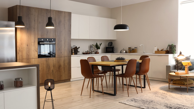 Ahşap dolaplar, ahşap masa ve kahverengi sandalyeler ve kolye aydınlatma ile modern yemek odası.