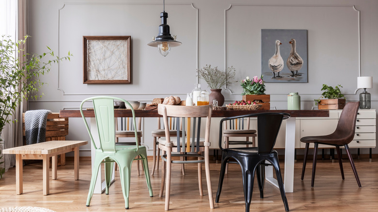 Ahşap masa, kolye aydınlatma ve çeşitli sandalye ile eklektik yemek odası.