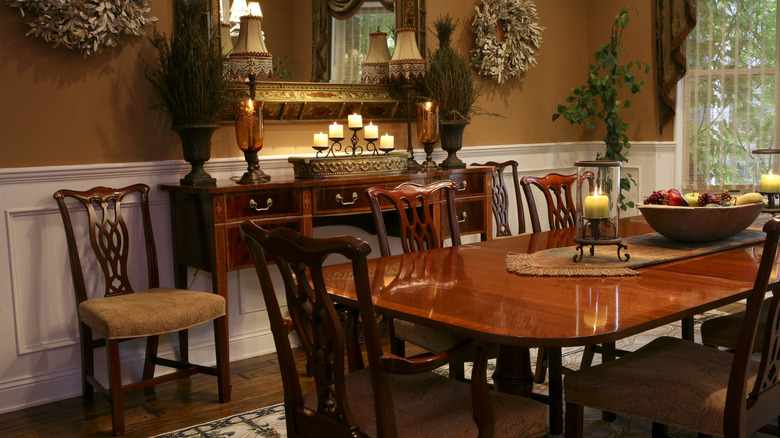 Koyu ahşap masa ve süslü sandalyeler, lambalar ve büyük bir ayna ile geleneksel yemek odası.