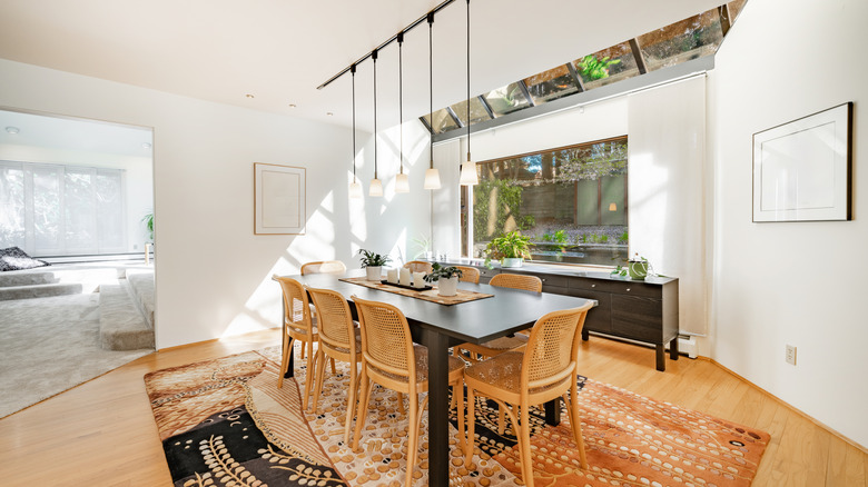 Basit bir masaya sahip İskandinav yemek odası, kolye aydınlatma ile tonozlu bir tavan, ahşap sandalyeler ve doğadan esinlenen bir halı.