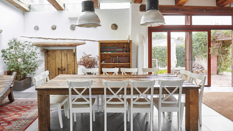 Büyük bir ahşap masa, beyaz sandalyeler ve doğal ışık ile Akdeniz mutfak ve yemek alanı.