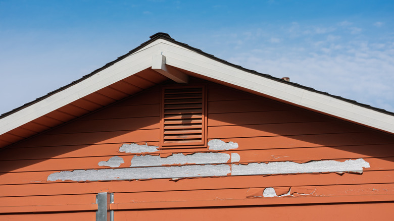 Çatı çizgisinin yakınında soyma boyası ile kırmızı ahşap bir dış duvarın kapatılması.