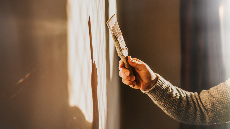 Bir duvarı boyayan ve boya fırçası tutan bir adam.