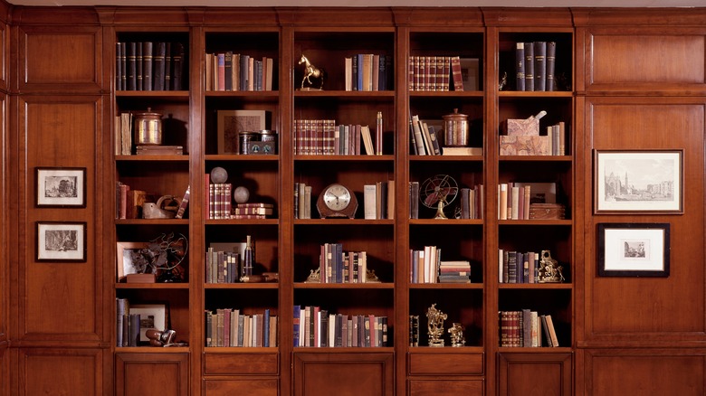 Kitap ve süslemelerle dolu bir ceviz kahverengi kitaplık.