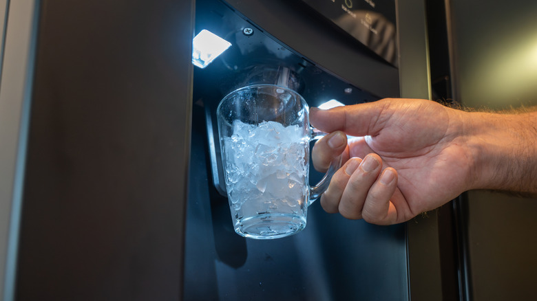 Buzdolabında buz dağıtıcısından buzlu bir bardak tutun.