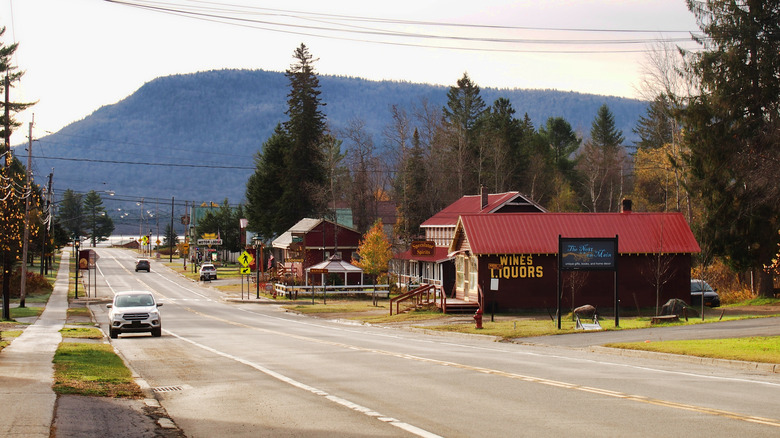 Birkaç bina ve kaldırım ile küçük bir şehir merkezinde arabalarla yol, arka planda dağ