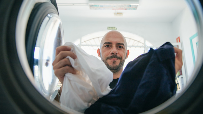 Adam çarşaflarını çamaşır makinesine yükler.