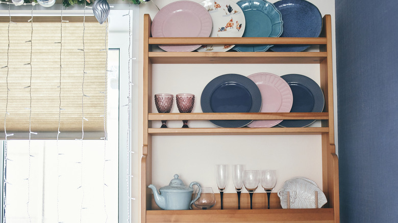 Süslü tabaklar ve bardaklar ile ahşap plaka rafı.