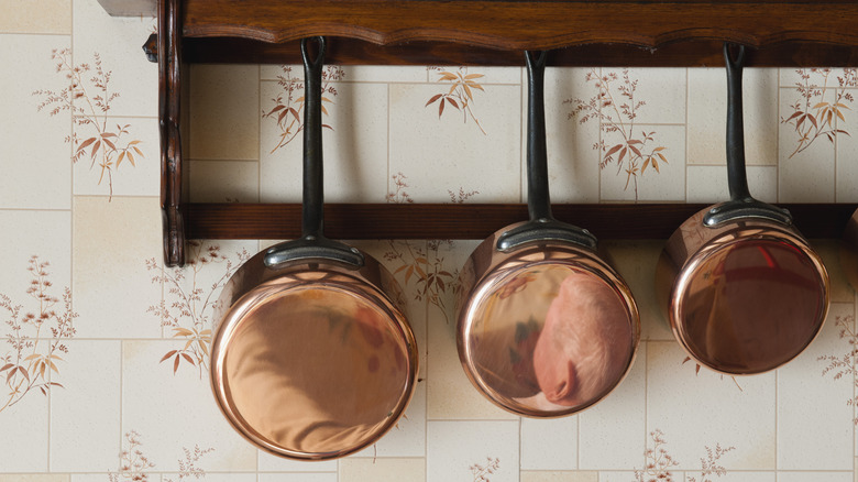 Ahşap bir raftan üç cilalı bakır tencere asılı